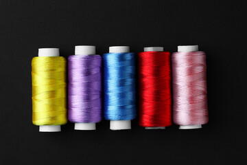 Spools of colorful sewing threads on black background, flat lay