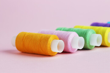 Spools of colorful sewing threads on pink background, closeup