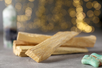 Palo santo sticks and gemstone on grey table against blurred lights, closeup