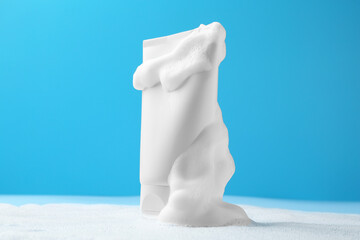 Tube of cosmetic product with foam on light blue background © New Africa