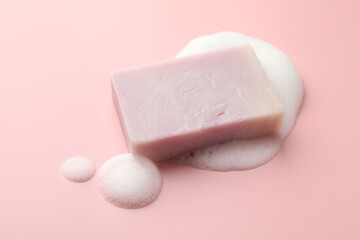 Soap bar with foam on light pink background, closeup