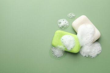 Soap bars with foam on green background, flat lay. Space for text