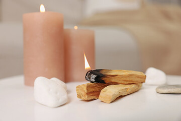 Palo santo sticks, burning candles and stones on white table indoors, closeup