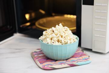 Tasty popcorn in bowl near microwave oven on light marble table, closeup