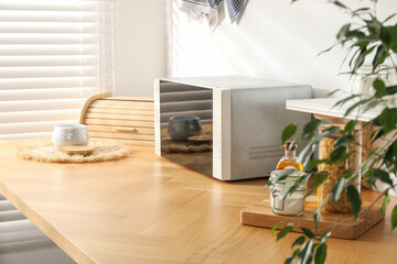 Closed microwave oven and kitchen utensils on wooden table indoors