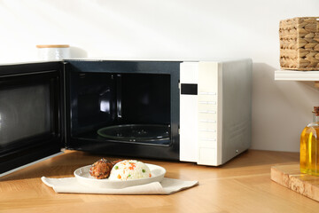 Open microwave oven with cooked rice and chicken on wooden table indoors