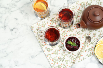 Glasses of tea in metal holders served on white marble table, flat lay