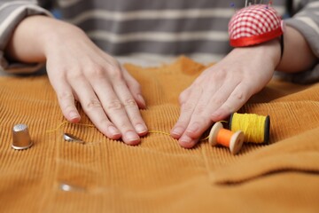 Woman working with cloth and spools of sewing threads at table, closeup