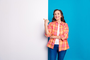 Smiling mature woman in a checkered shirt gesturing happily against dual-color background, showing...