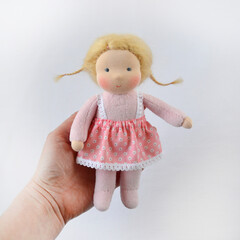 Person holding Waldorf doll in pink dress with cheerful expression on white background