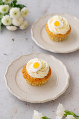 Lemon Poppy Seed Cupcakes with lemon curd and cream cheese topping and Fried Egg candies. Colourful Easter eggs, flowers on a stone background, top view. Easter holiday and festive food.