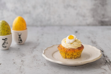 Lemon Poppy Seed Cupcakes with lemon curd and cream cheese topping and Fried Egg candies. Colourful Easter eggs, flowers on a stone background, top view. Easter holiday and festive food.