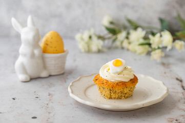 Lemon Poppy Seed Cupcakes with lemon curd and cream cheese topping and Fried Egg candies. Colourful Easter eggs, flowers on a stone background, top view. Easter holiday and festive food.