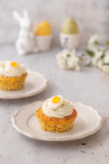 Lemon Poppy Seed Cupcakes with lemon curd and cream cheese topping and Fried Egg candies. Colourful Easter eggs, flowers on a stone background, top view. Easter holiday and festive food.