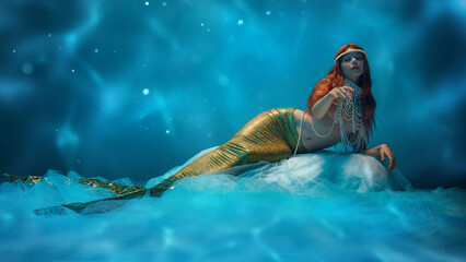 Ethereal woman, mermaid with long red hair and shimmering tail resting in an enchanting blue...