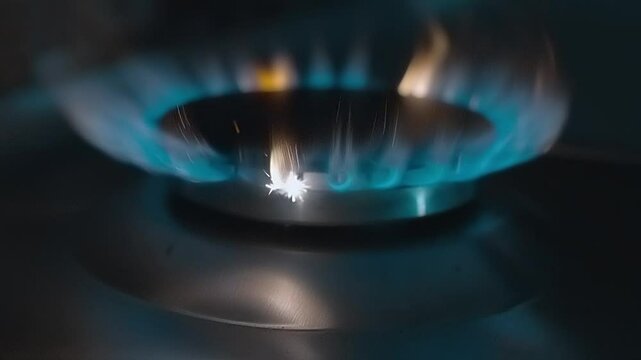 In the kitchen, in the dark on the stove, the gas ignites with a lot of sparks on a large and powerful burner consisting of two rings. Shot in motion. Closeup. Macro. Slow mo, slow motion
