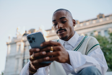 well-dressed Black man looks at his phone with a serious, focused expression. Sitting outdoors in a...