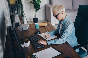 Focused Woman Working on Computer and Writing Notes in Modern Office Interior