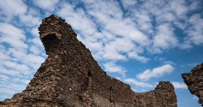 26.02.2025 Siria, Arad County, Romania. Time lapse of Siria castle ruins. Partially standing stone wall, looking up pov, daytime, blue sky, passing clouds, no people