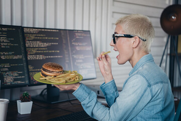 Young professional programmer enjoying a meal while working in a modern home office with daylight