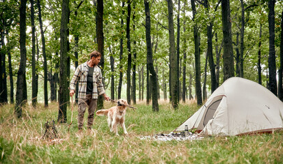 A man is camping in the beautiful forest alongside his loyal dog, enjoying natures tranquility