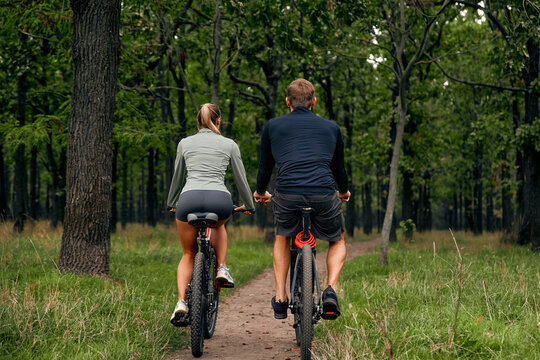A couple joyfully biking together on a lush green forest path during a beautiful summer day