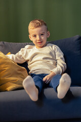 Fototapeta premium Blond boy relaxing on sofa with white socks and green background
