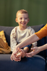 Mother giving foot massage to smiling son on sofa