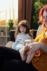 Mother massaging daughter's feet on sofa at home: family bonding