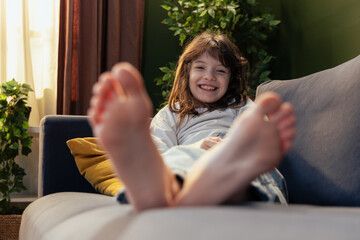 Smiling girl relaxing on sofa with feet up: showing happiness and comfort at home