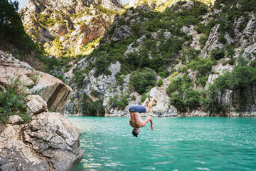 A young man jumps from a cliff on the Verdon mountain lake on a summer day.