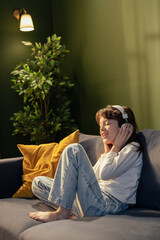 Obraz premium Young girl enjoying music with headphones on sofa at home