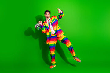 Young man in a colorful rainbow-striped suit posing enthusiastically on bright green background...