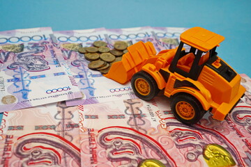 Excavator with tenge coins on the background of tenge banknotes of different denominations