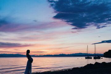 Fototapeta premium Expecting mother enjoying a serene sunset by the water with boats