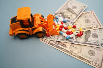 Fototapeta premium Euro banknotes and an excavator loading a handful of capsule tablets. Pharmaceutical business. Medicines. Spending on healthcare.