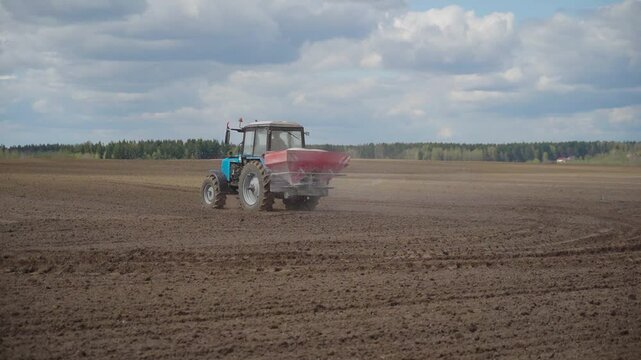 Farmer with agricultural machinery fertilizing agricultural field in spring time