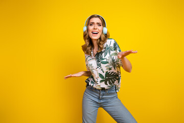 Cheerful young woman wearing headphones and enjoying music on a vibrant yellow background, expressing positive energy.