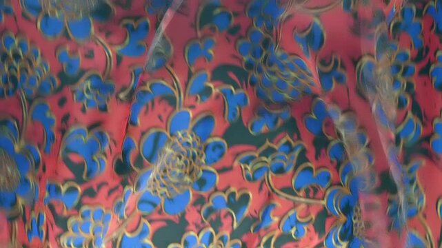 Red fabric with beautiful blue floral pattern falls, fluttering on a black background. Closeup. Macro. Slow mo, slow motion, high speed camera, 200fps