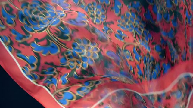 Red fabric with beautiful blue floral pattern falls, fluttering on a black background. Closeup. Macro. Slow mo, slow motion, high speed camera, 200fps