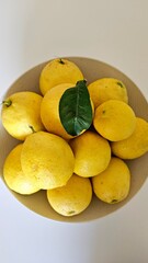 Close-up of fresh lemons in a bowl, with a single green leaf, capturing the vibrant color and freshness of citrus fruit.