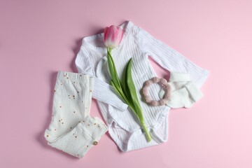 Baby clothes, socks, teether and tulip flower on pink background, flat lay