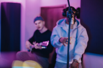 Two musicians collaborate in a professional recording studio filled with vibrant, colorful...