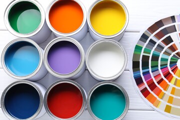 Cans of bright paints and color palettes on white wooden table, flat lay
