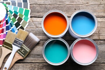 Cans of bright paints, brushes and color palettes on wooden table, flat lay