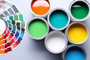 Cans of bright paints and color palettes on grey background, flat lay