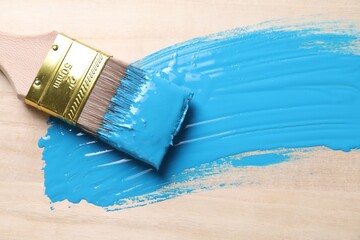 Smear of light blue paint and brush on wooden table, top view