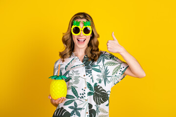 Cheerful young woman in tropical outfit featuring a vibrant pineapple design showing the thumbs-up...