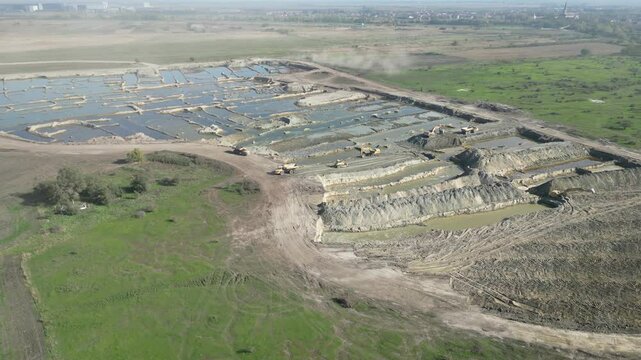 Aerial drone view of quarry and sand mining site with conveyor belts, excavators, storage piles and artificial lakes surrounded by rural agricultural landscape 