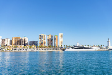 Fototapeta premium Stunning view of Málaga's waterfront showcasing modern buildings, a yacht, and the iconic La Farola lighthouse.